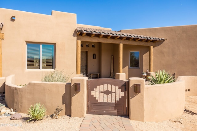 adobe home featuring a tile roof, a gate, fence, and stucco siding