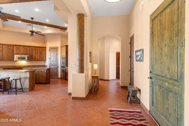 kitchen with light tile patterned floors, a ceiling fan, a towering ceiling, appliances with stainless steel finishes, and brown cabinets