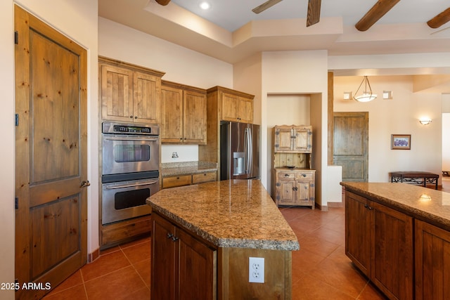 kitchen with appliances with stainless steel finishes, brown cabinets, ceiling fan, and dark tile patterned floors