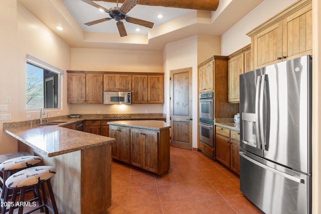 kitchen with light stone counters, stainless steel appliances, a peninsula, tile patterned floors, and a tray ceiling