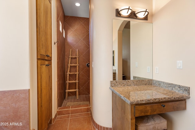 full bath featuring tile patterned flooring, a tile shower, and vanity