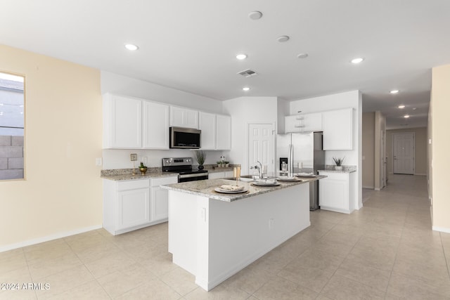 kitchen with light stone countertops, a center island with sink, white cabinets, and stainless steel appliances