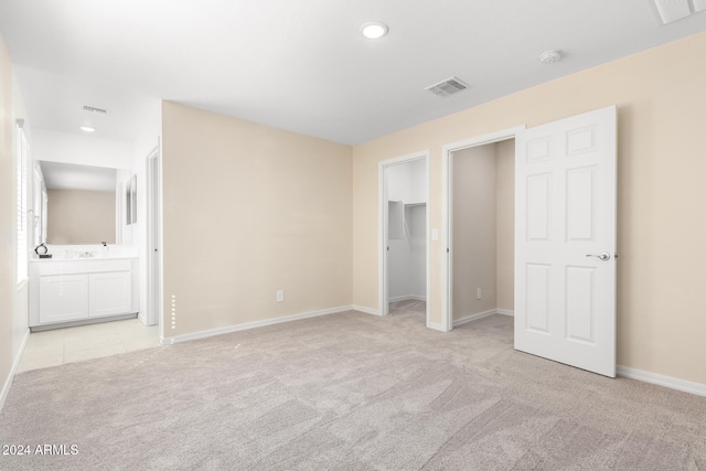 unfurnished bedroom featuring a spacious closet, light carpet, connected bathroom, and a closet