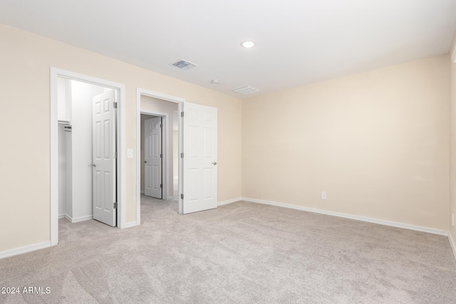 unfurnished bedroom with light carpet, a spacious closet, and a closet