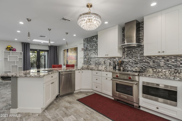 kitchen with wall chimney exhaust hood, white cabinets, stainless steel appliances, and pendant lighting