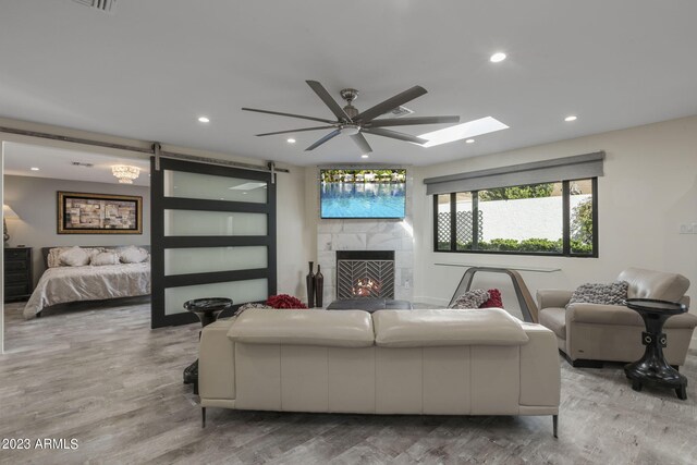 living room featuring light hardwood / wood-style flooring, a barn door, a tiled fireplace, and ceiling fan