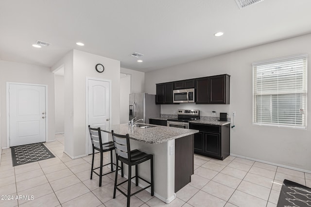 kitchen with a breakfast bar, a center island with sink, sink, stainless steel appliances, and light stone countertops