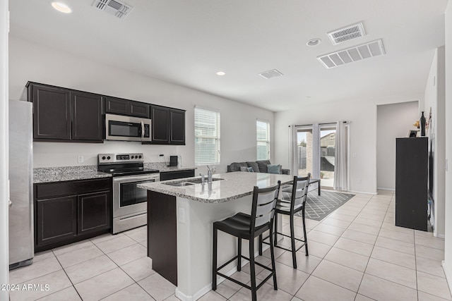 kitchen featuring light stone counters, light tile patterned floors, a kitchen island with sink, appliances with stainless steel finishes, and a breakfast bar area