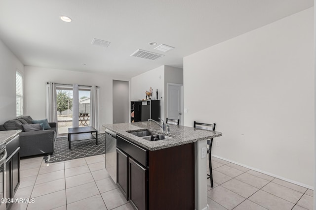 kitchen featuring a kitchen island with sink, sink, dark brown cabinets, light tile patterned floors, and dishwasher