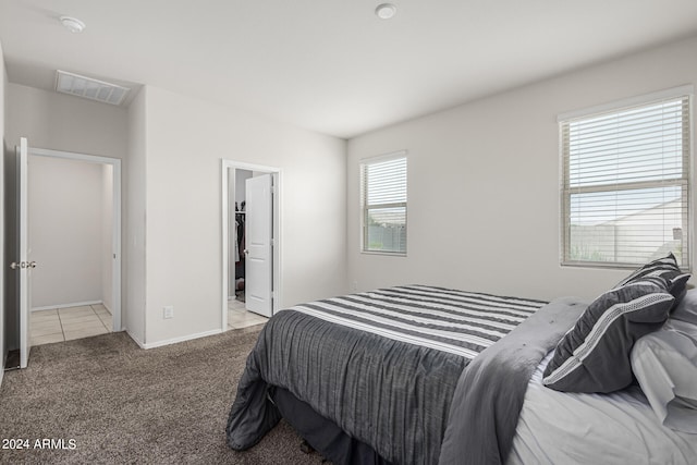 bedroom with light carpet, ensuite bath, multiple windows, and a walk in closet