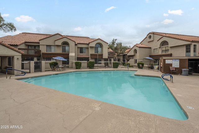 community pool featuring fence, a patio, and a residential view