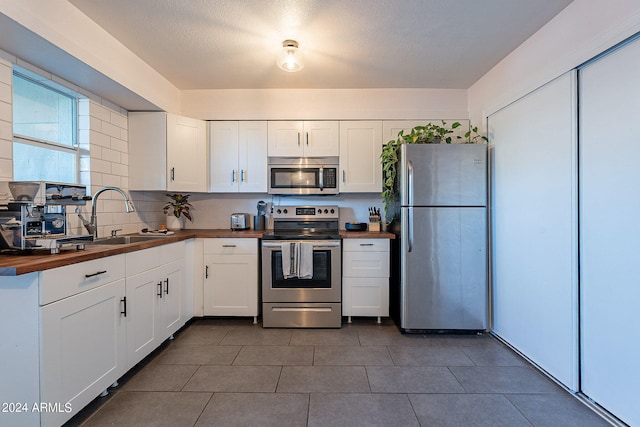 kitchen featuring white cabinetry, butcher block countertops, stainless steel appliances, dark tile patterned floors, and sink