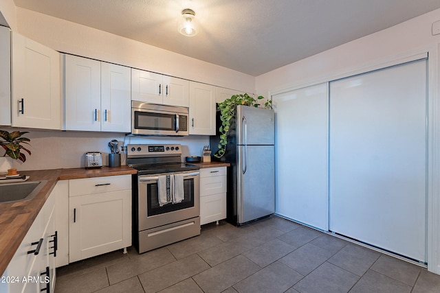 kitchen with dark tile patterned floors, a textured ceiling, white cabinetry, appliances with stainless steel finishes, and wood counters