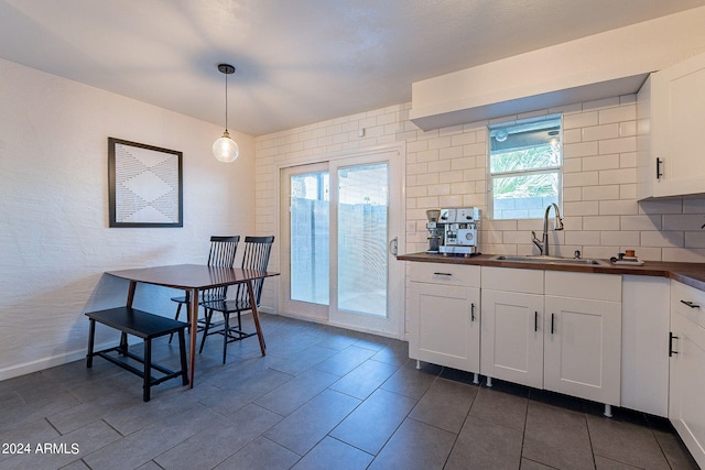 kitchen featuring a healthy amount of sunlight, hanging light fixtures, sink, and white cabinets