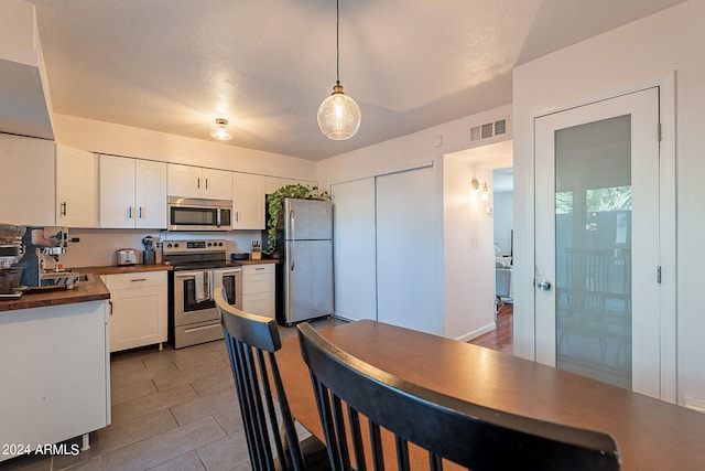 kitchen with hanging light fixtures, butcher block countertops, a textured ceiling, white cabinetry, and appliances with stainless steel finishes