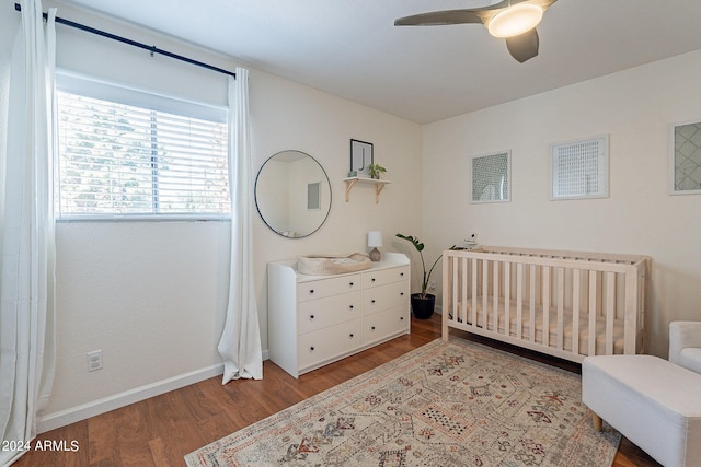 bedroom with a crib, hardwood / wood-style floors, and ceiling fan