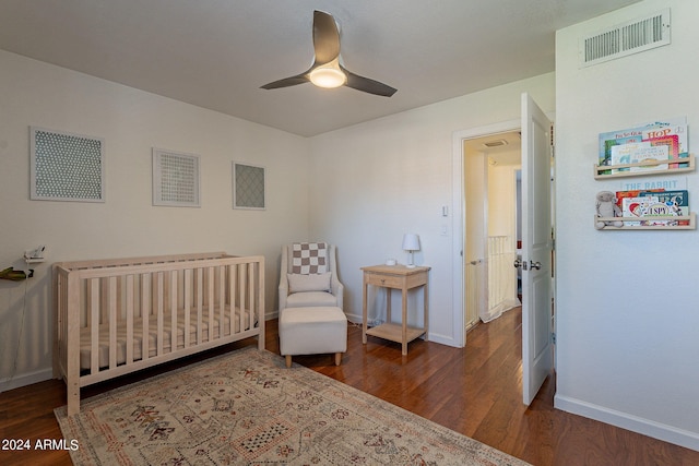 bedroom featuring ceiling fan, a crib, and dark hardwood / wood-style floors