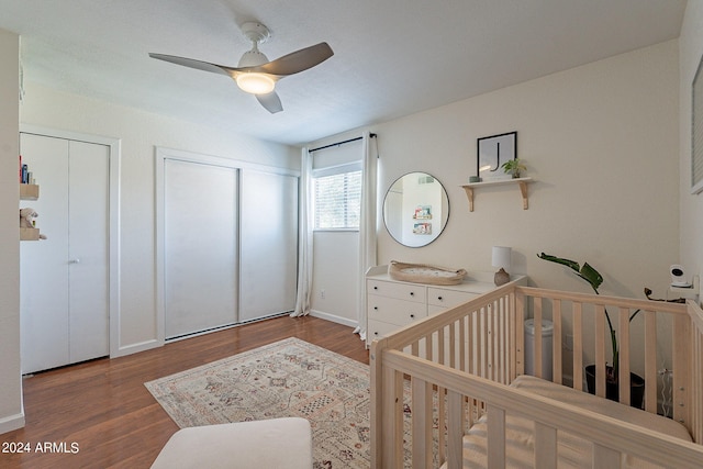 bedroom featuring a crib, two closets, ceiling fan, and wood-type flooring