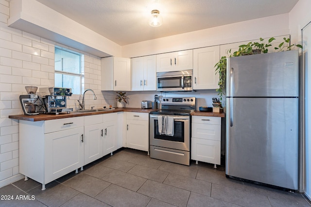 kitchen with white cabinets, sink, stainless steel appliances, and wooden counters