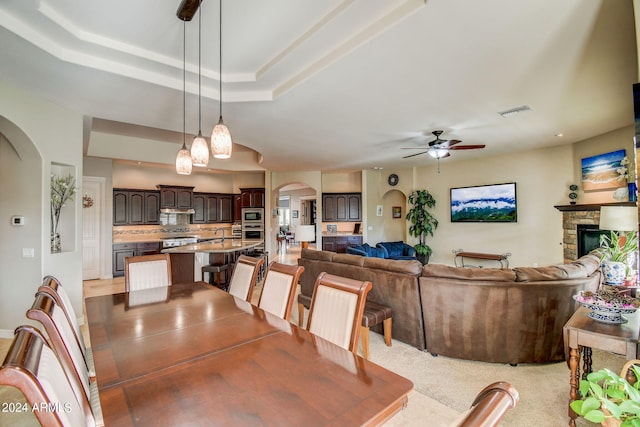 dining space with light carpet, ceiling fan, a raised ceiling, and a fireplace