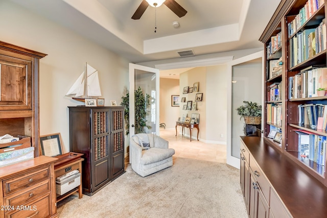 living area featuring light colored carpet, ceiling fan, and a raised ceiling