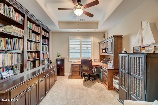 home office with light colored carpet, ceiling fan, and a raised ceiling