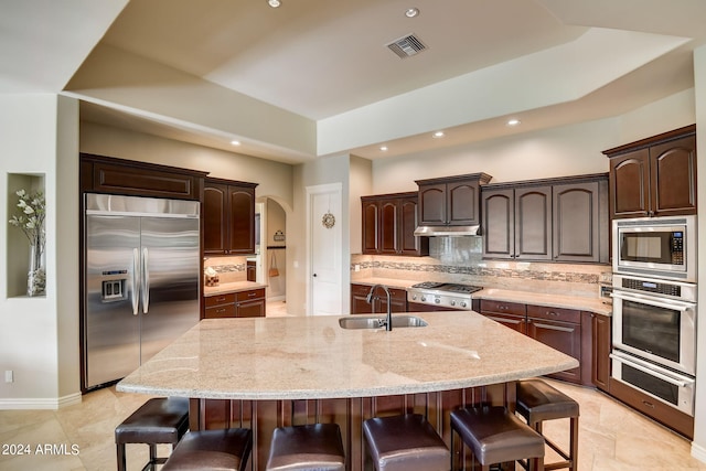 kitchen featuring built in appliances, sink, tasteful backsplash, and a kitchen island with sink