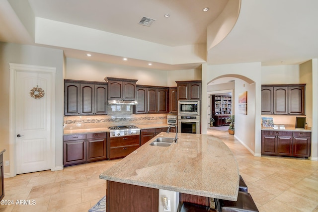 kitchen with backsplash, stainless steel appliances, a center island with sink, light tile floors, and sink