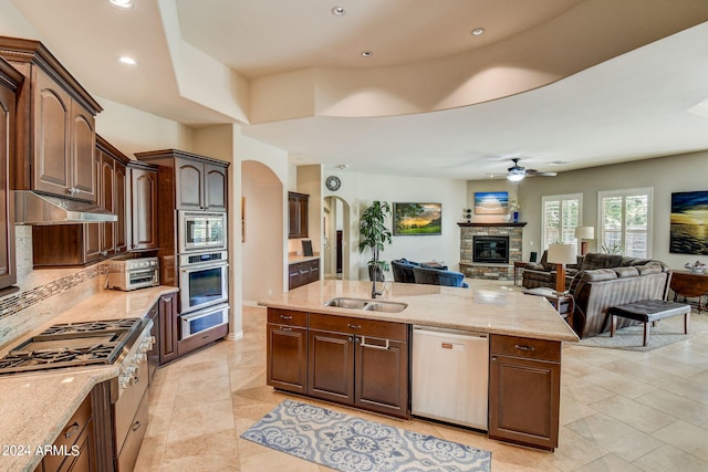 kitchen featuring a stone fireplace, ceiling fan, stainless steel appliances, sink, and light tile floors