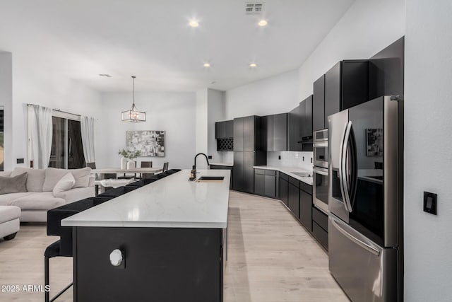 kitchen with sink, appliances with stainless steel finishes, a spacious island, tasteful backsplash, and decorative light fixtures