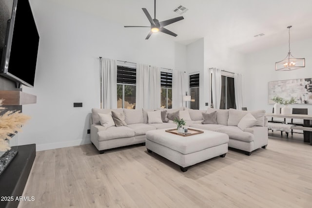 living room featuring ceiling fan with notable chandelier, light hardwood / wood-style floors, and a high ceiling