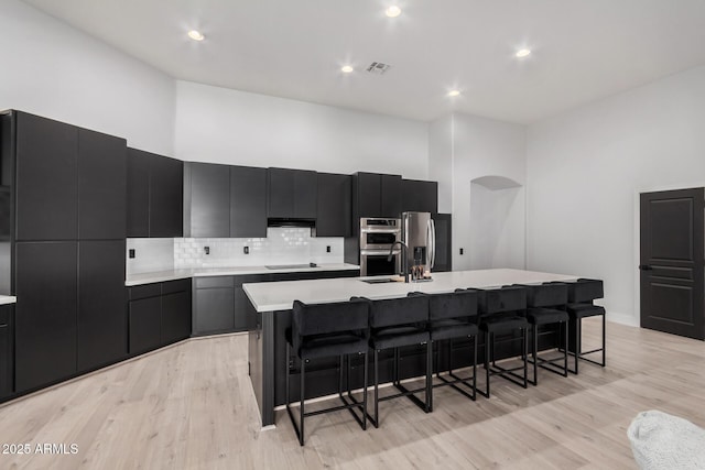 kitchen featuring a towering ceiling, appliances with stainless steel finishes, an island with sink, and a breakfast bar area