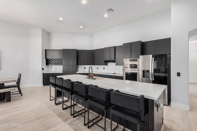 kitchen featuring a towering ceiling, stainless steel appliances, a large island, and a breakfast bar