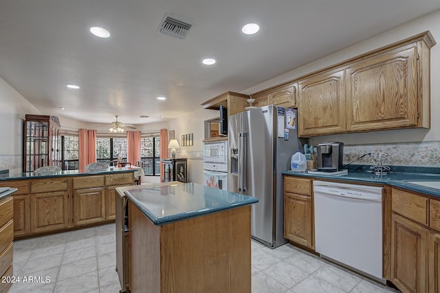 kitchen featuring white appliances, visible vents, brown cabinetry, dark countertops, and a center island