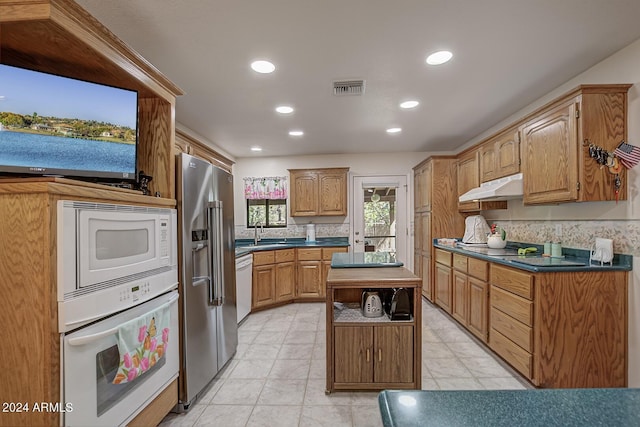 kitchen featuring under cabinet range hood, white appliances, a sink, visible vents, and dark countertops