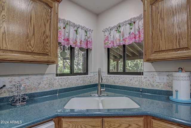 kitchen with dishwasher, brown cabinetry, dark countertops, and a sink