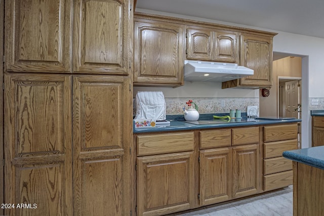 kitchen featuring stovetop, dark countertops, brown cabinets, and under cabinet range hood