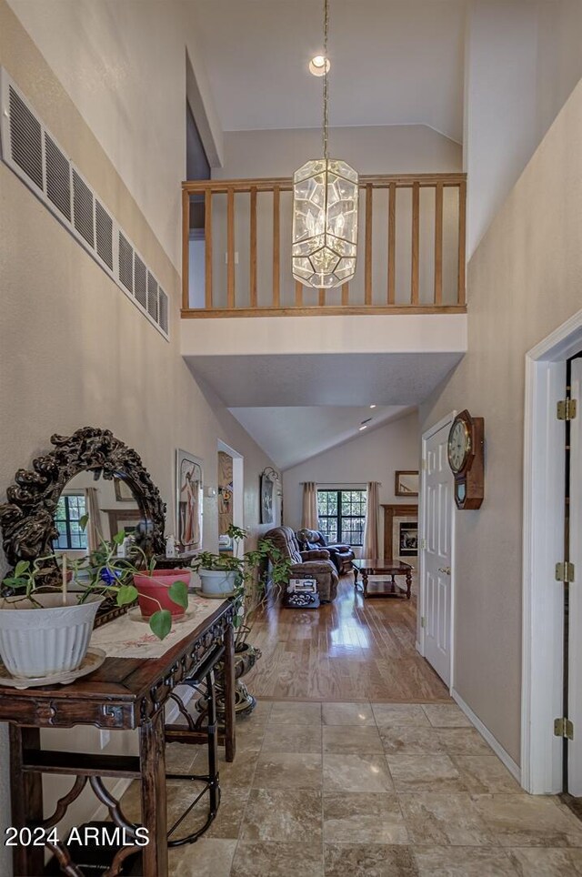 entryway featuring a chandelier, high vaulted ceiling, a fireplace, visible vents, and baseboards