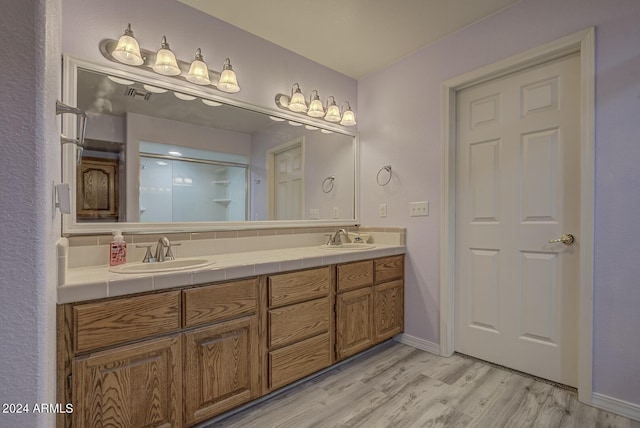 full bathroom with double vanity, visible vents, a sink, and wood finished floors