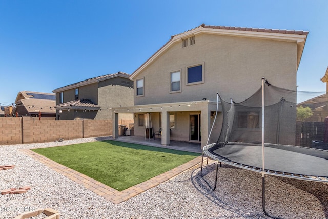 23848 W Grove St, Buckeye, AZ 85326 - rear view of house with a trampoline, a lawn, a fenced backyard, a patio, and stucco siding
