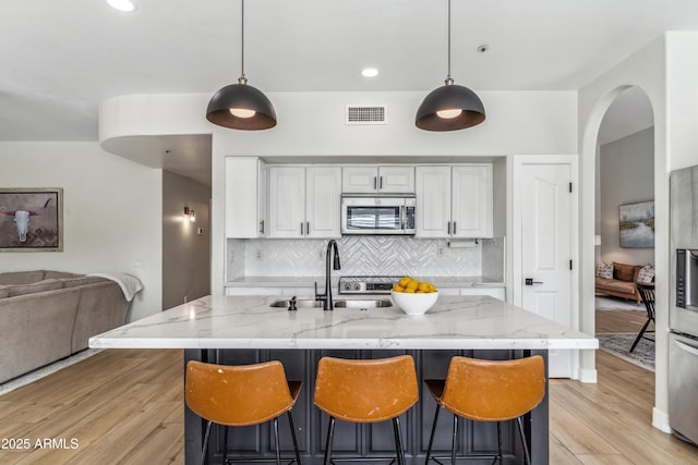 kitchen with sink, appliances with stainless steel finishes, light stone counters, and decorative light fixtures