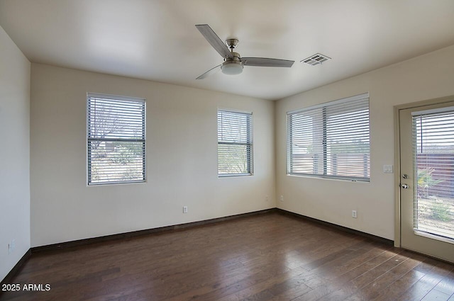 spare room featuring dark wood-style floors, ceiling fan, visible vents, and baseboards