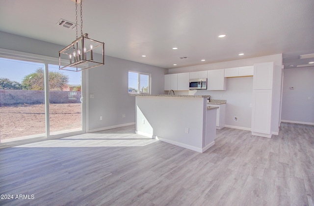 kitchen with stainless steel microwave, white cabinetry, light wood-type flooring, and visible vents