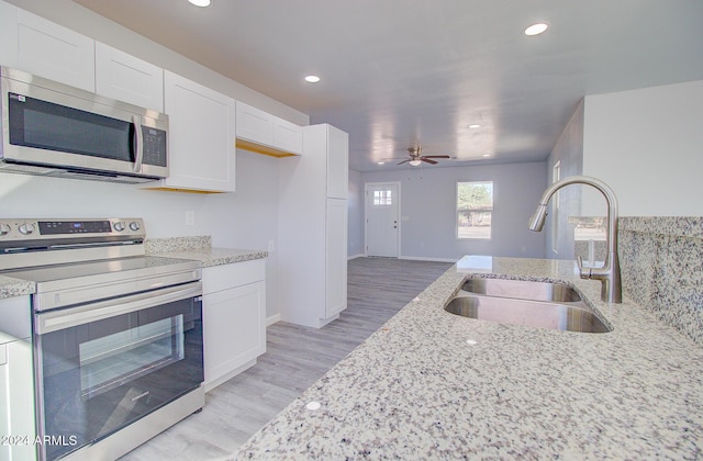 kitchen featuring a sink, white cabinetry, light wood-style floors, appliances with stainless steel finishes, and light stone countertops