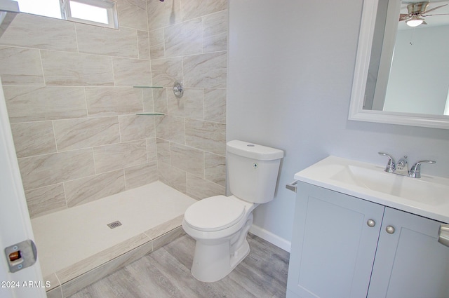 bathroom with toilet, wood finished floors, a tile shower, baseboards, and vanity