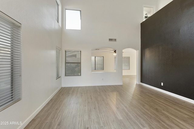 unfurnished living room featuring ceiling fan, light hardwood / wood-style floors, and a high ceiling