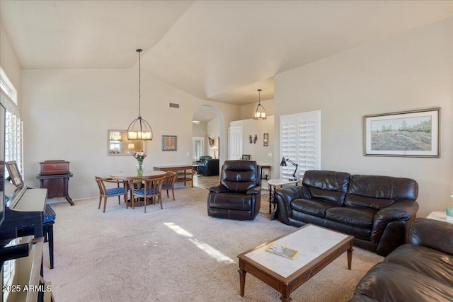 carpeted living room with high vaulted ceiling, arched walkways, visible vents, and a notable chandelier