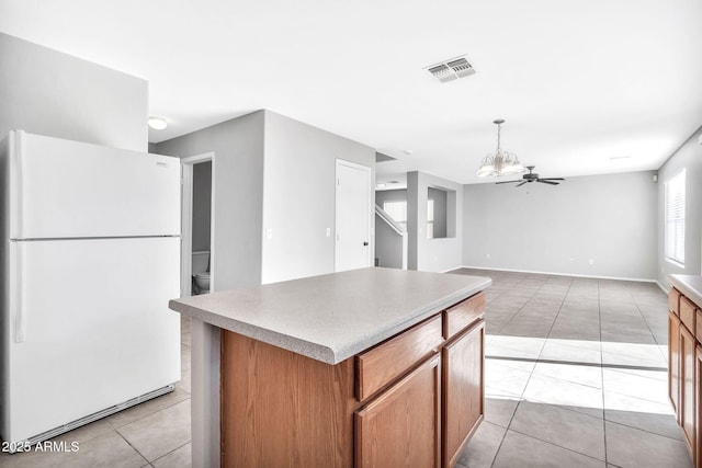 kitchen with light tile patterned floors, white refrigerator, pendant lighting, a kitchen island, and ceiling fan with notable chandelier