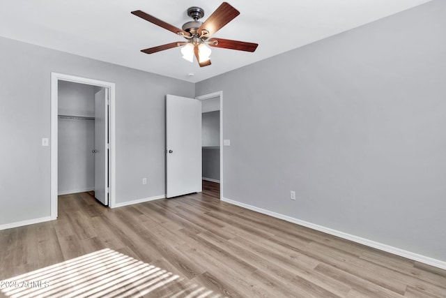 unfurnished bedroom with ceiling fan, a spacious closet, light hardwood / wood-style floors, and a closet