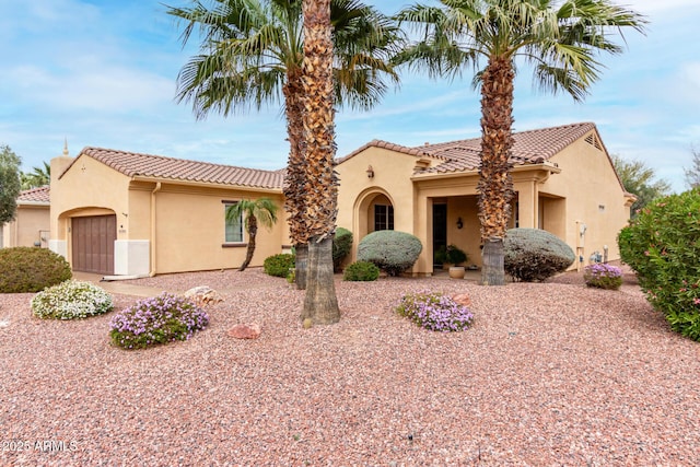 mediterranean / spanish home with an attached garage, a tile roof, and stucco siding